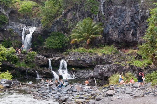 A scenic waterfall surrounded by lush greenery, with people enjoying the water and rocky shoreline.
