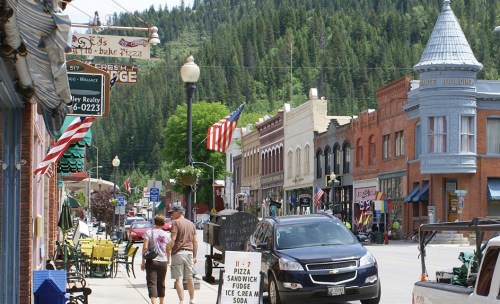 A charming small-town street lined with shops, flags, and mountains in the background on a sunny day.