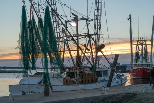 Fishing boats docked at sunset, with nets hanging and a colorful sky reflecting on the water.