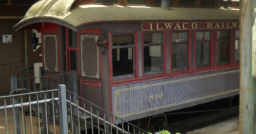 Historic Ilwaco Railway train car displayed at a station, featuring red and purple wooden exterior and large windows.