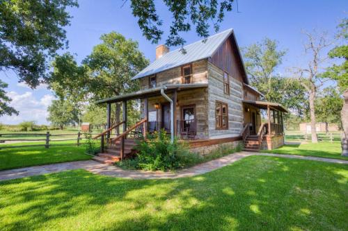A charming two-story house with a wooden exterior, surrounded by green grass and trees under a clear blue sky.