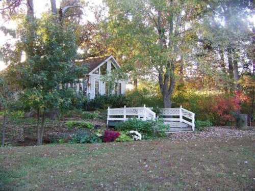 A quaint house surrounded by trees and colorful foliage, featuring a white deck and lush garden.