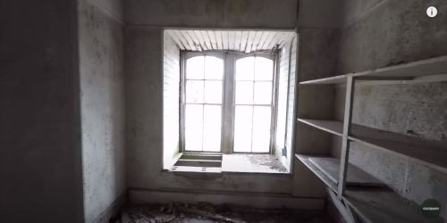 Abandoned room with a dusty window and empty shelves, featuring peeling walls and debris on the floor.