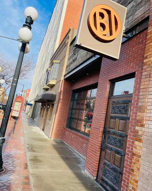 Exterior of a brick building with a large sign reading "BI" and a decorative wooden door, on a sunny day.