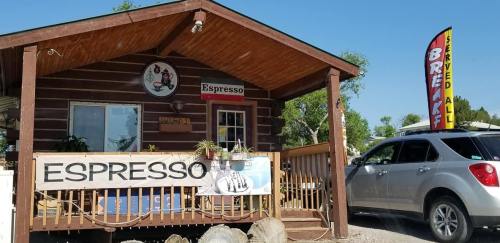 A cozy log cabin coffee shop with a sign reading "Espresso" and a car parked nearby. Bright sunny day.