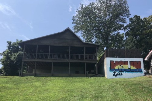 A wooden cabin with a porch, set on a grassy area, next to a colorful mural that reads "Molin Lake."
