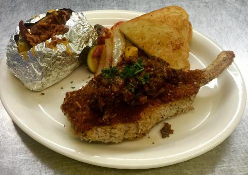 A plate featuring a breaded pork chop with sauce, a baked potato, and mixed vegetables.