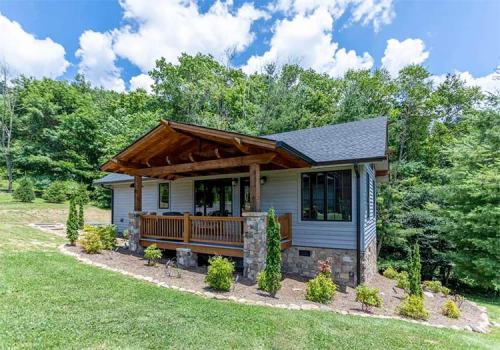 A charming single-story house with a wooden porch, surrounded by greenery and trees under a blue sky.
