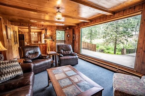 Cozy wooden living room with leather chairs, a coffee table, and large windows overlooking a forested area.