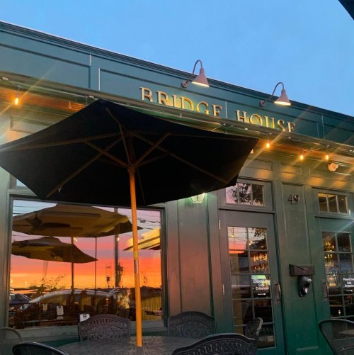 Exterior of Bridge House restaurant at sunset, featuring a black umbrella and warm lighting.