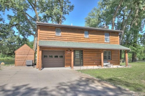 A two-story log cabin with a garage, surrounded by trees and a clear blue sky.