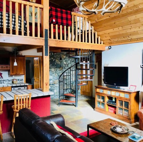 Cozy cabin interior featuring a spiral staircase, wooden beams, and a lofted sleeping area with rustic decor.