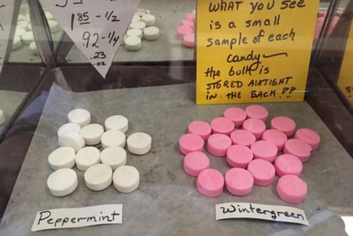 Display of white peppermint and pink wintergreen candies in a glass case, labeled with descriptions.