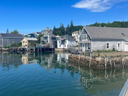 A serene waterfront scene featuring charming houses and reflections on calm water under a clear blue sky.