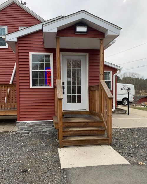 A red building with a wooden staircase and an "OPEN" sign in the window, set in a gravel area.