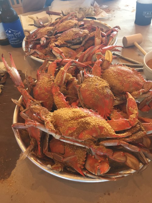 Two large platters filled with seasoned crabs, with a bottle of beer in the background.