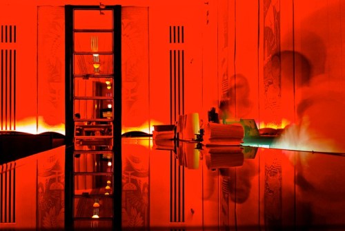 A dimly lit room with red lighting, featuring a mirrored surface and a tall, narrow window reflecting shadows.