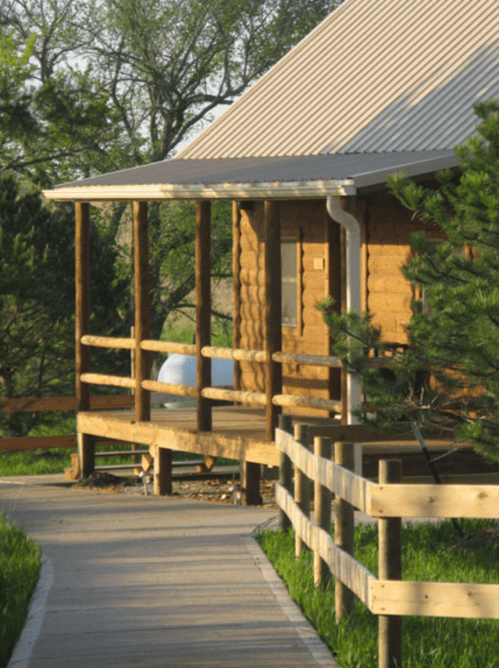 A wooden cabin with a porch, surrounded by greenery and a pathway leading to it.