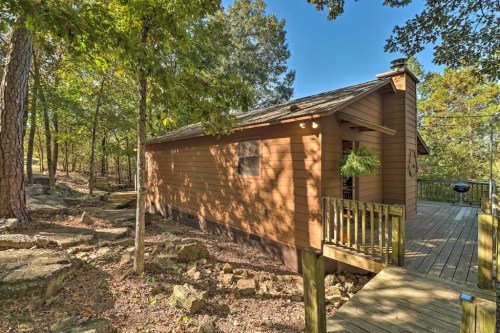A cozy wooden cabin surrounded by trees, featuring a deck and stone landscaping.