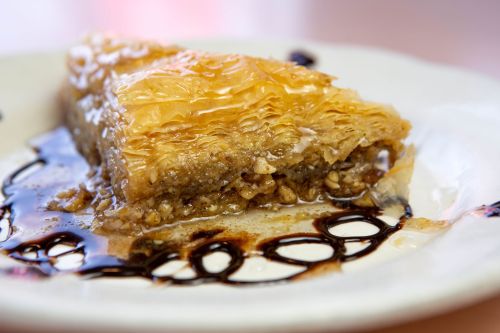 A slice of baklava drizzled with syrup on a white plate, showcasing its flaky layers and nut filling.