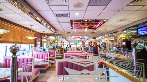 A vibrant diner interior with pink booths, neon lights, and a bustling atmosphere.