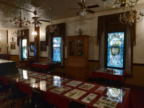 A vintage room with stained glass windows, chandeliers, and a long table displaying various artifacts and documents.