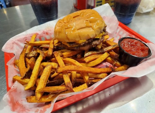 A basket of golden French fries with a cheeseburger and a small cup of ketchup on the side.