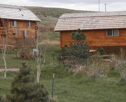 Two wooden cabins surrounded by grass and small trees, set against a hilly landscape under a cloudy sky.