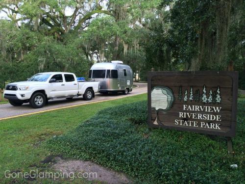 A silver Airstream trailer is parked next to a white pickup truck at Fairview Riverside State Park entrance.