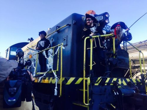 A decorated train with people in pirate costumes and skeletons, celebrating a festive event outdoors.