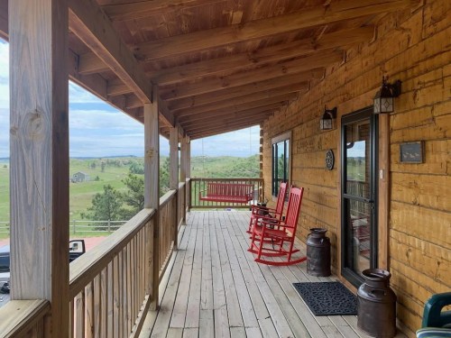 A wooden porch with red rocking chairs, overlooking a green landscape under a cloudy sky.