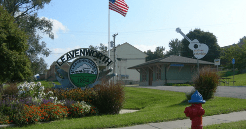 Welcome sign for Leavenworth, Kansas, with flowers, a flag, and a guitar-shaped sign for Melissa Etheridge.