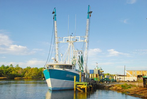 A fishing boat named "Integrity" docked at a pier under a clear blue sky, surrounded by trees and buildings.