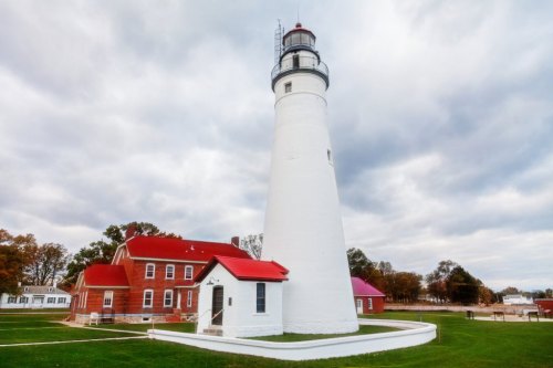 A tall white lighthouse beside a red-roofed building, set against a cloudy sky and green grass.