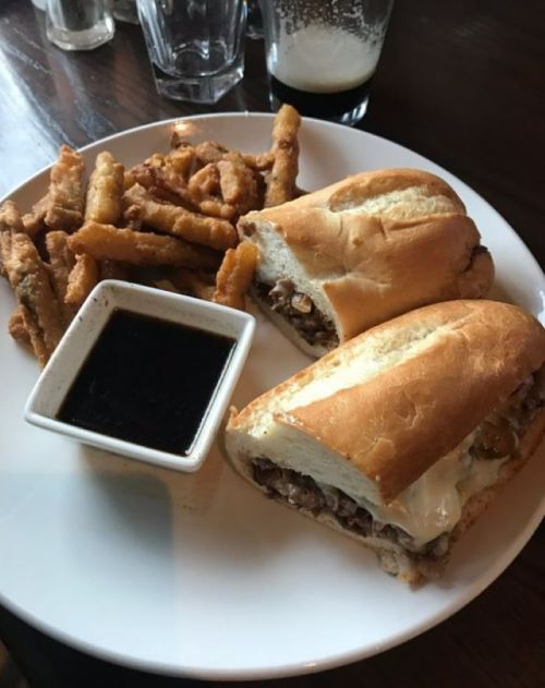 A plate with two sandwiches filled with meat and cheese, served with a side of fries and a small dish of dipping sauce.