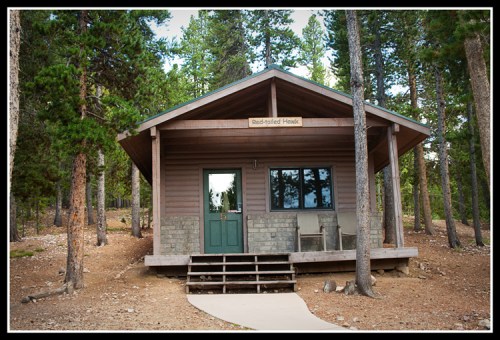 A rustic cabin named "Red-Polled Hawks" surrounded by tall trees and a gravel path.