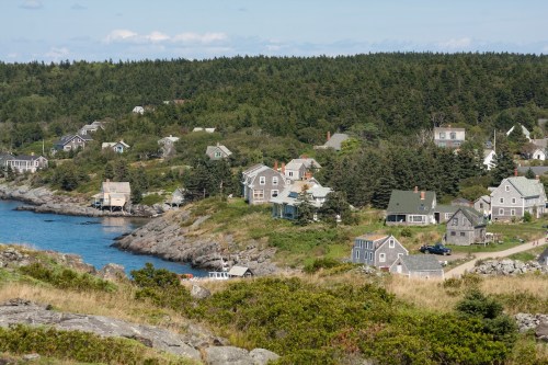 A scenic coastal view of a small village with houses nestled among trees and rocky shores by the water.