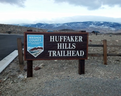 Sign for Huffaker Hills Trailhead in Washoe County, with mountains in the background and a cloudy sky.