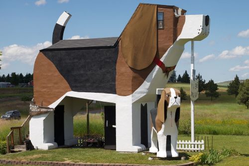 A large, whimsical dog-shaped building with a smaller dog statue in front, set against a grassy landscape.