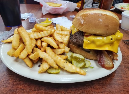 A plate with a cheeseburger topped with bacon and pickles, served with a side of crispy French fries.
