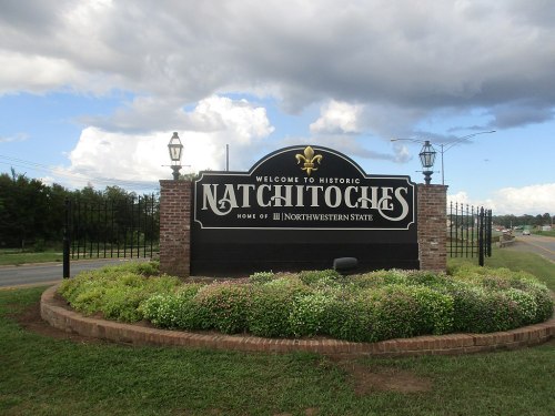 Welcome sign for Natchitoches, Louisiana, featuring decorative elements and surrounded by greenery.
