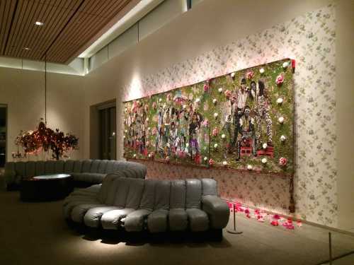 A modern lounge with a curved gray sofa and a large, colorful wall art piece featuring flowers and figures.