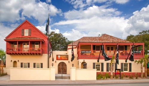 A colorful building with red and beige walls, featuring balconies and pirate-themed flags, under a blue sky.