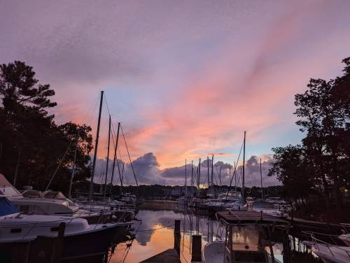 A serene marina at sunset, with boats docked and colorful clouds reflecting in the water.