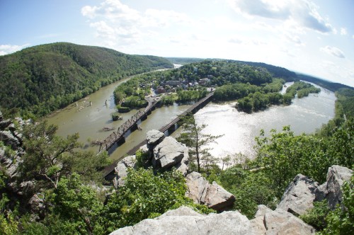 A panoramic view of a river winding through green hills, with a bridge and a small town visible in the distance.
