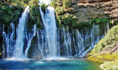 A scenic waterfall cascading over rocky cliffs into a clear blue pool, surrounded by lush greenery.