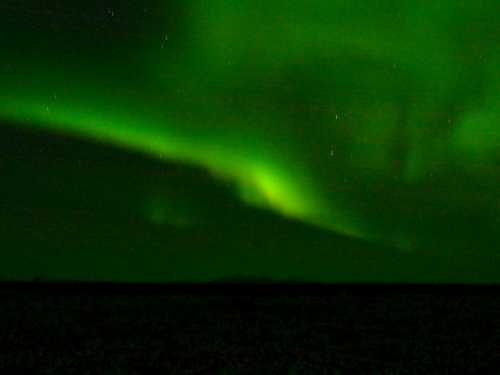 A vibrant green aurora borealis dances across a dark night sky, illuminating the horizon.