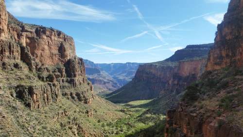 A scenic view of a canyon with steep rock formations and a clear blue sky, showcasing lush greenery below.