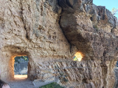 Two natural rock formations with openings, illuminated by sunlight, set against a rugged cliffside.
