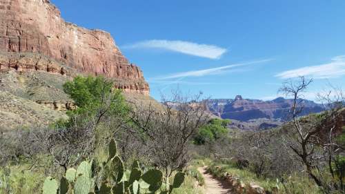 A scenic trail winds through a desert landscape with red rock formations and sparse vegetation under a clear blue sky.